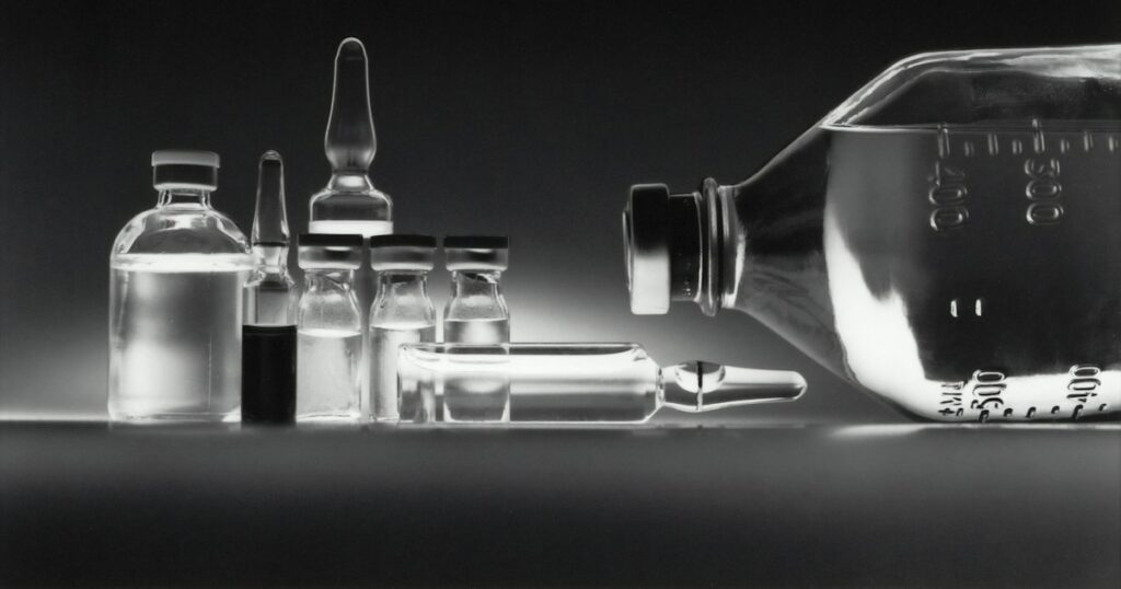 Glass pharmaceutical vials and an infusion bottle on a dark surface