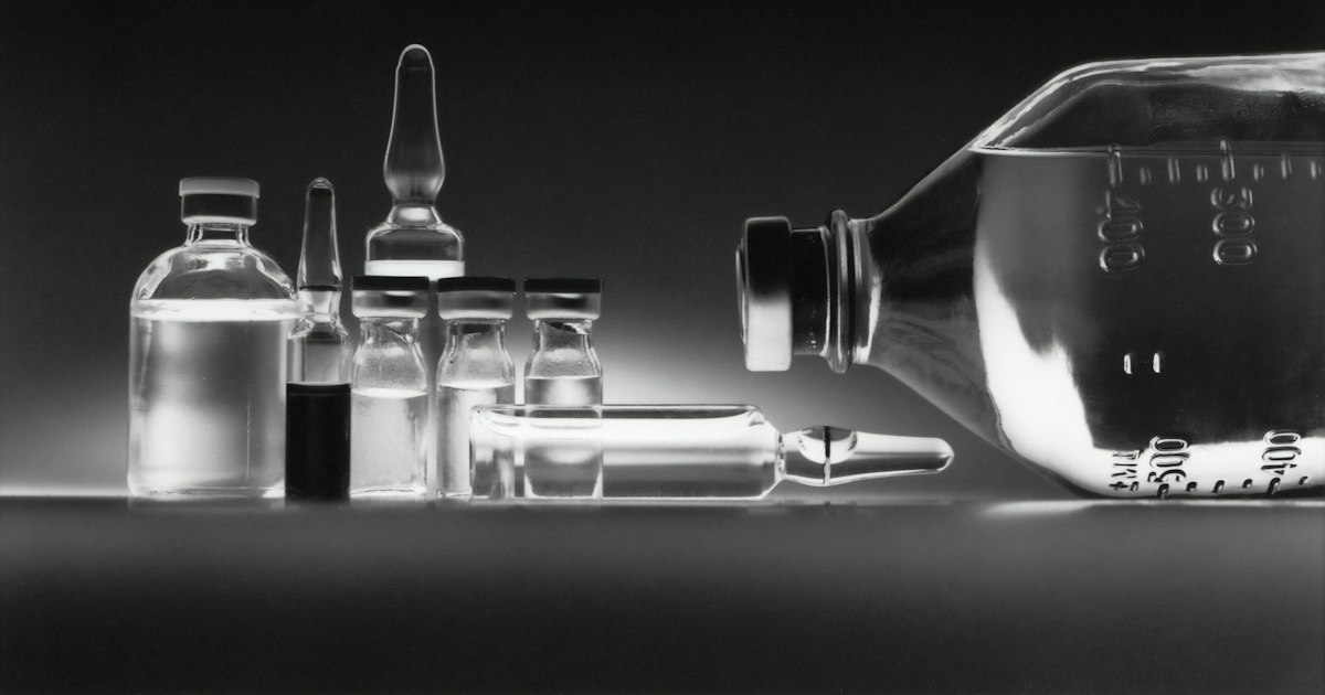 Glass pharmaceutical vials and an infusion bottle on a dark surface