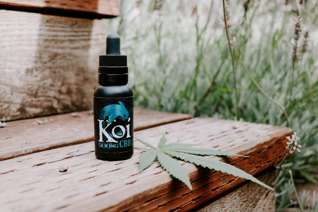 CBD oil bottle with dropper next to a hemp leaf outdoors