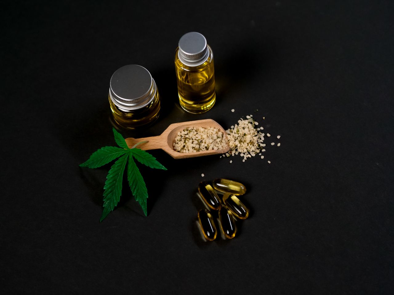 Cannabis oil and capsules with hemp seeds and a leaf on a dark backdrop