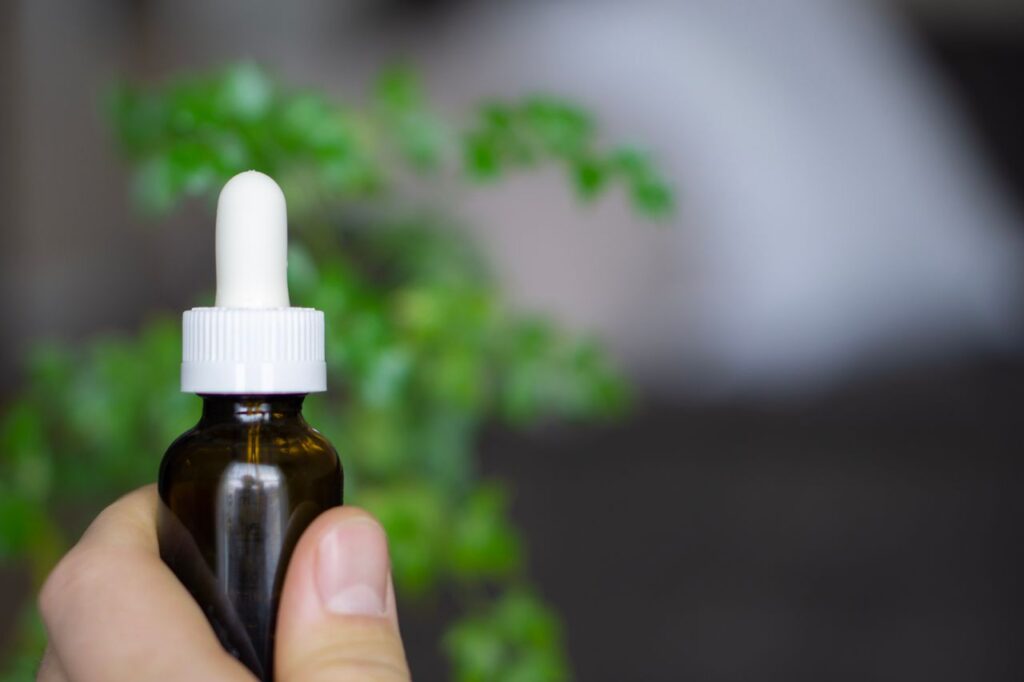 Hand holding a dropper bottle of CBD oil against a botanical background