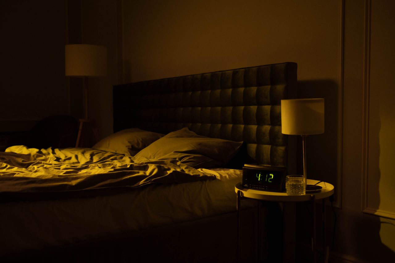 Dimly lit bedroom with an unmade bed and a digital clock