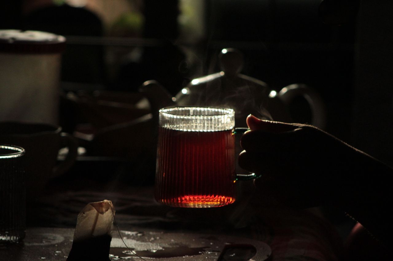 Hand holding a steaming cup of herbal tea in low light