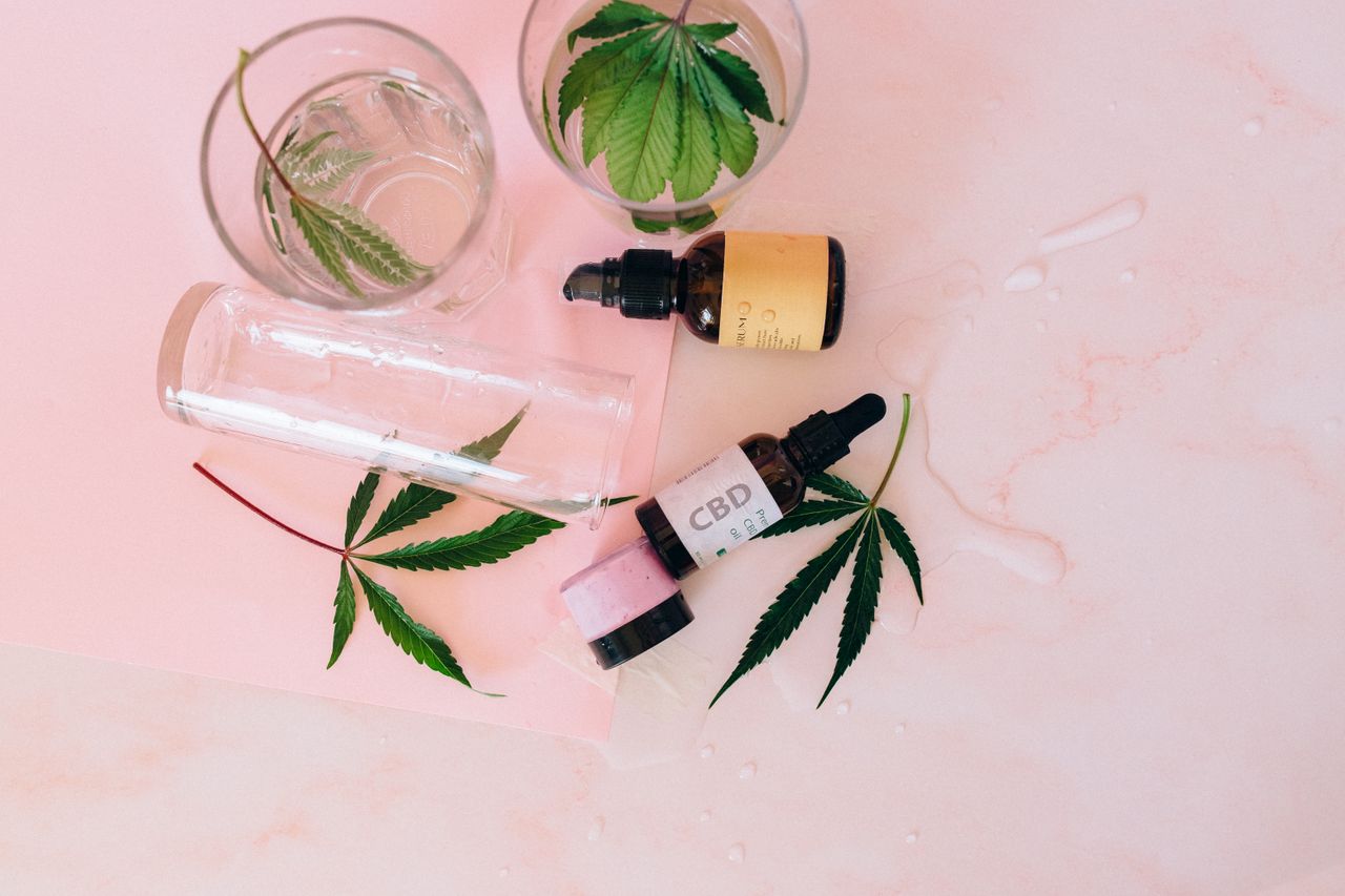 CBD oil bottles and cannabis leaves on a pink surface