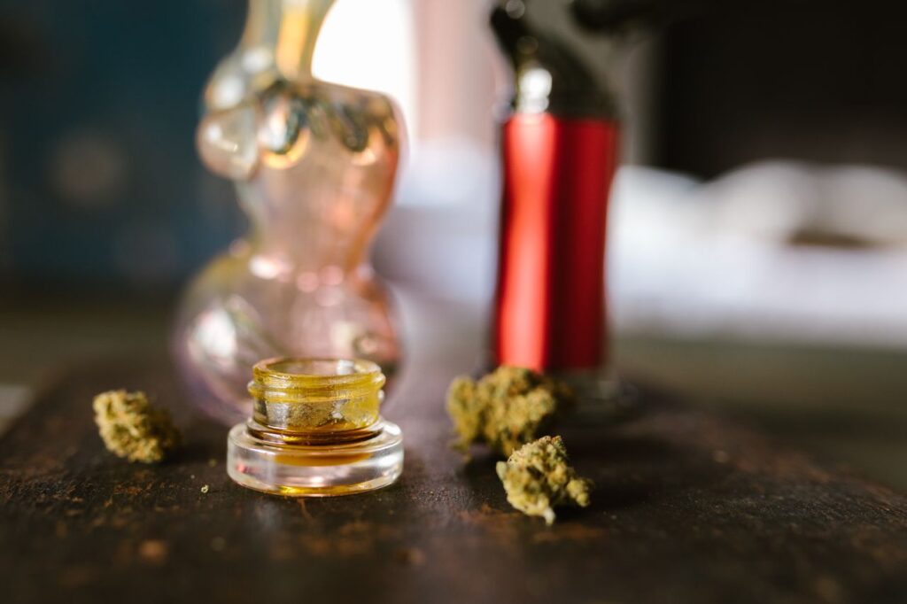 Glass jar of cannabis concentrate surrounded by dried buds