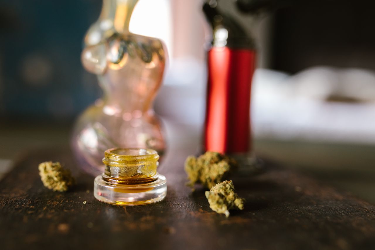 Glass jar of cannabis concentrate surrounded by dried buds