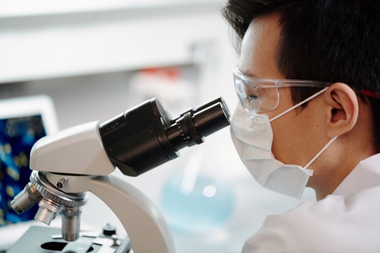 Scientist in a mask examining samples through a microscope
