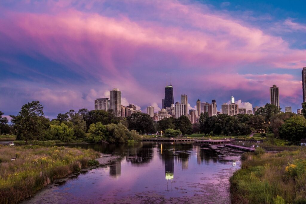 Vibrant sunset over Chicago skyline with reflections in a tranquil pond, surrounded