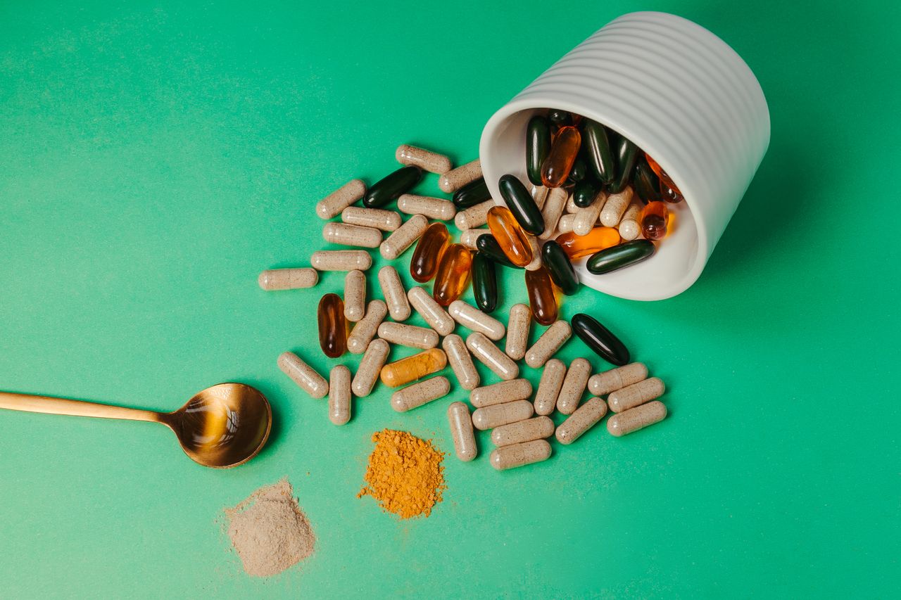 Capsules, pills and powder on a green background with a spoon
