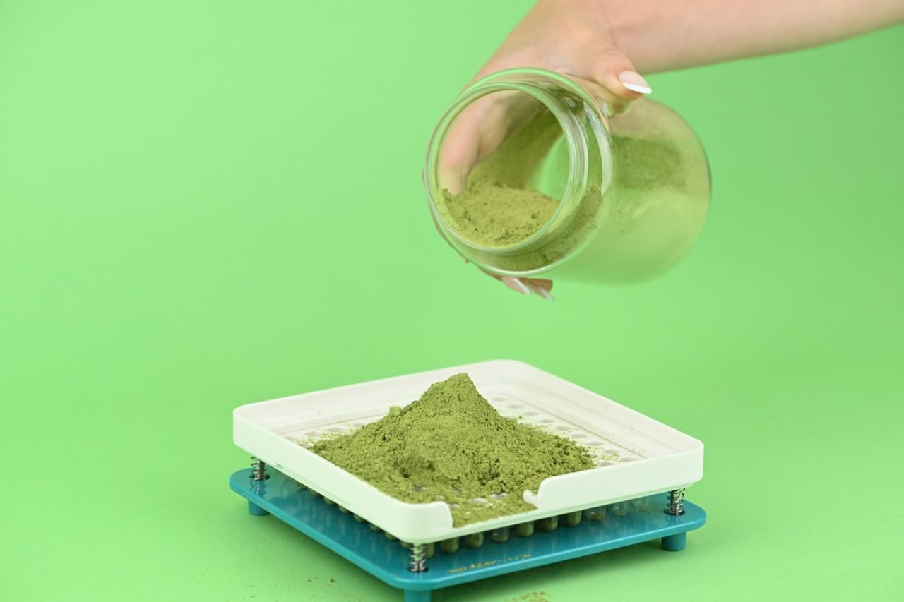 Green herbal powder poured into a capsule filling machine