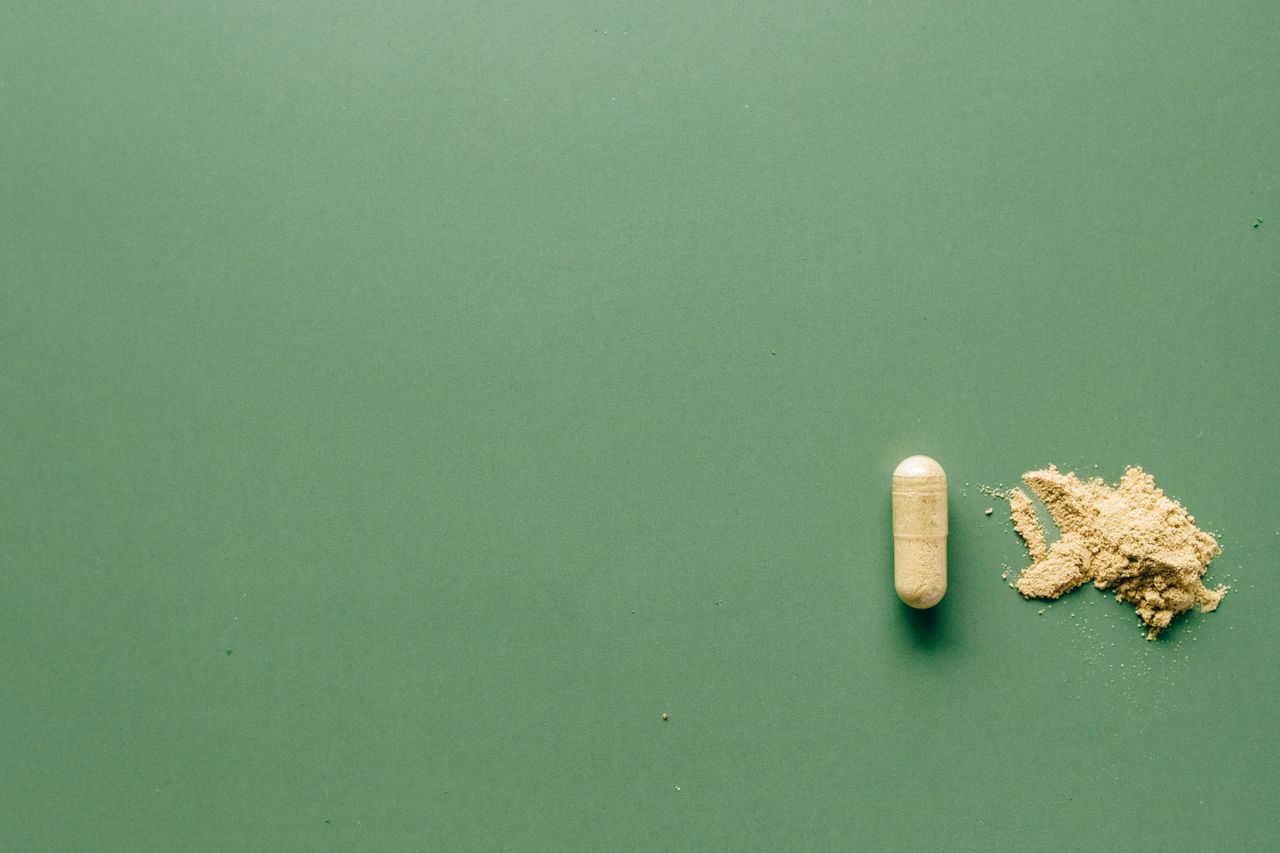Herbal supplement capsule and powder on a green surface