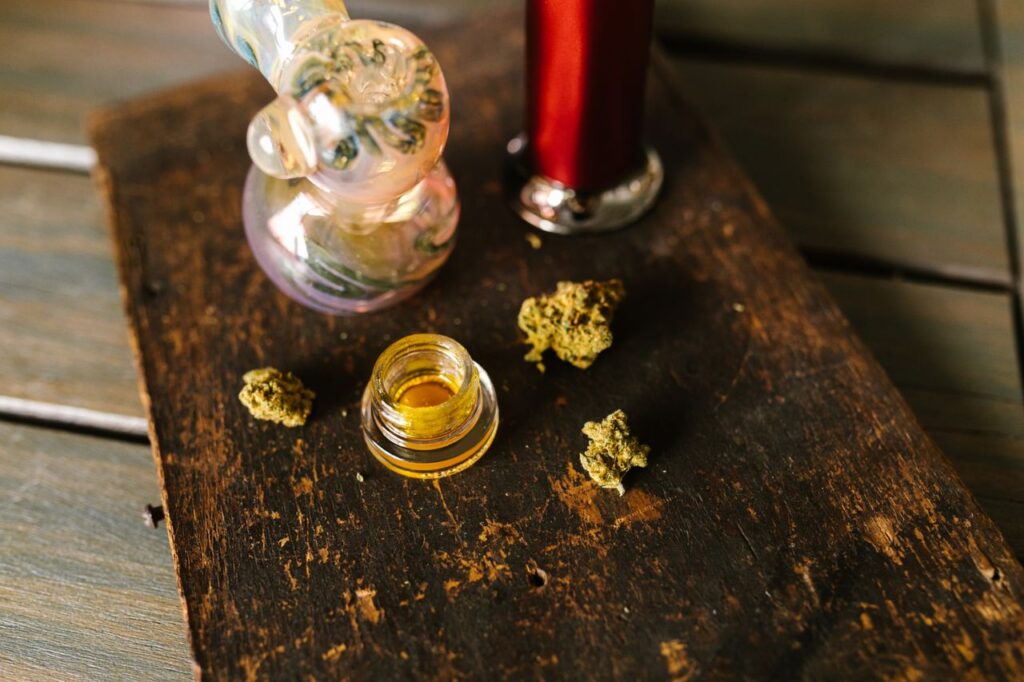 Cannabis buds, a glass pipe and wax concentrate on a wooden surface