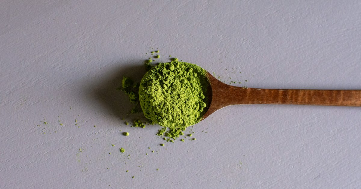 Green botanical powder in a wooden spoon