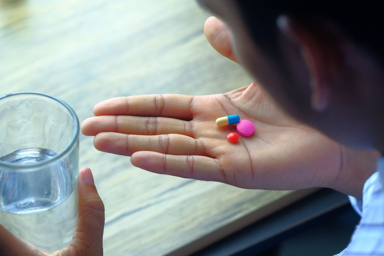 Person holding pills in their palm next to a glass of water