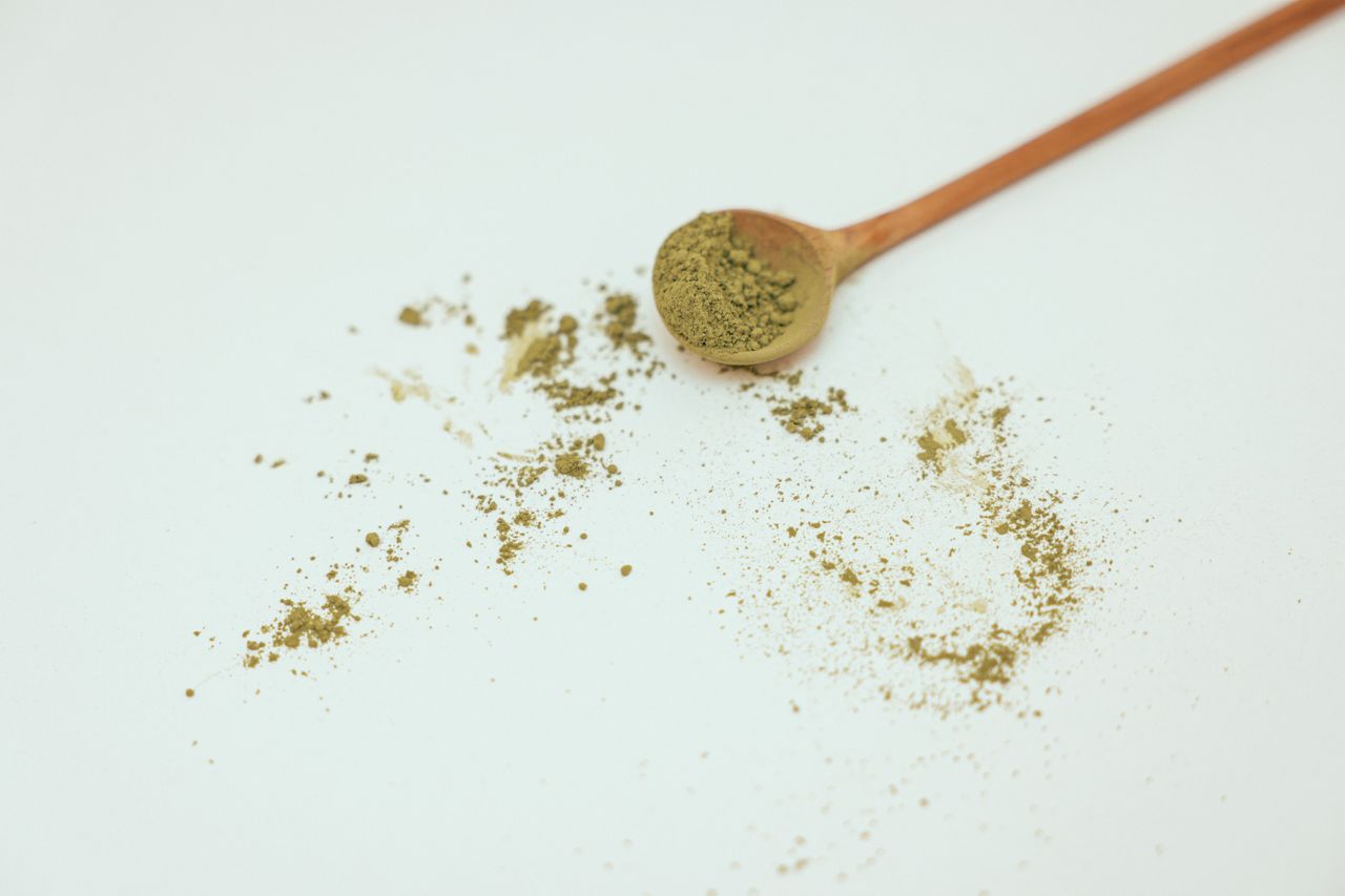 Green powder with a wooden spoon on a white surface