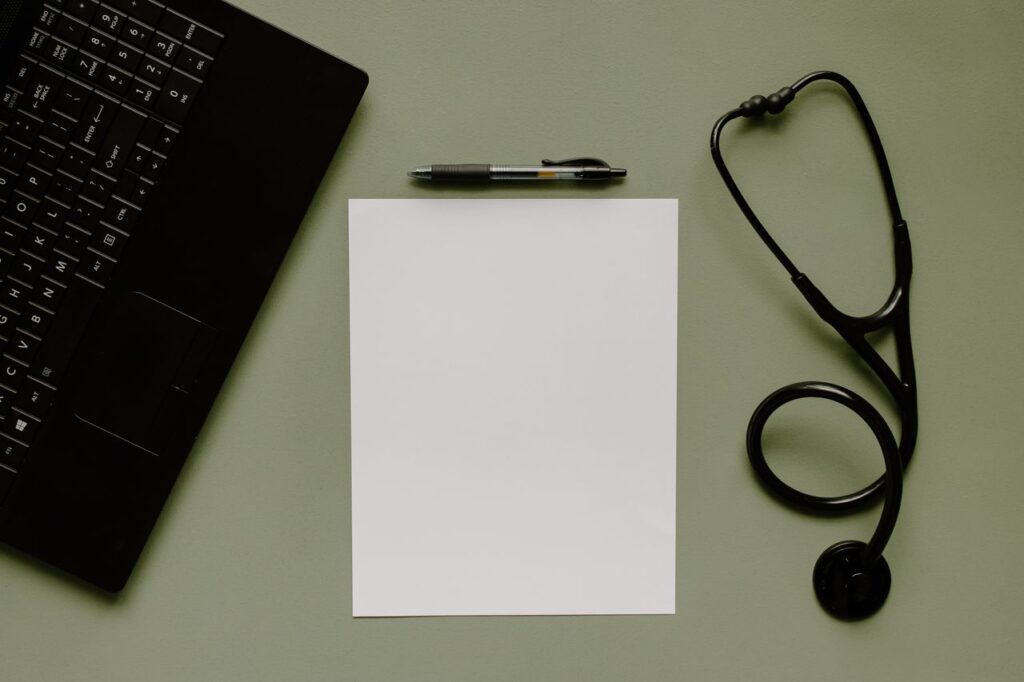 Medical workspace with blank paper, a stethoscope and a laptop