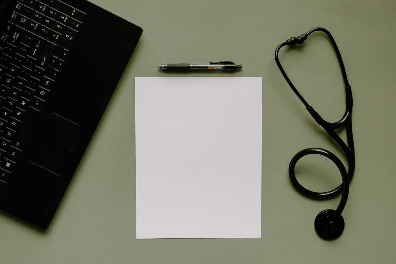Medical workspace with blank paper, a stethoscope and a laptop