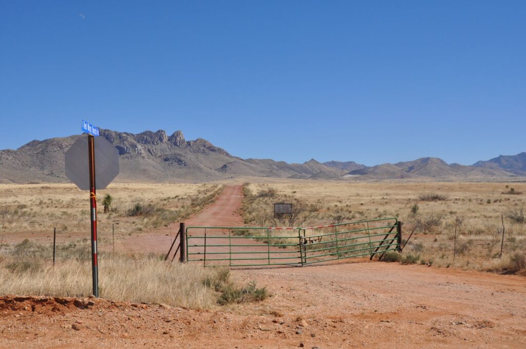 Dirt road leading to mountains in Valentine, TX, USA with a fence and clear blue